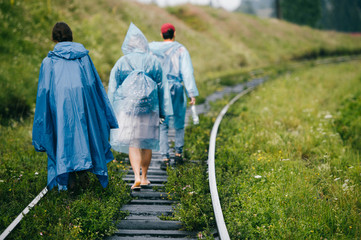 Couple of young rebel lovers travelers in raincoats walking in danger zone on railroad outdoor at nature. Company of friends rest on vacation. Tourist clothes. Hipster lifestyle. Warning. Occurence.