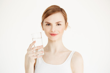 Young beautiful girl with perfect skin smiling looking at camera holding glass of water over white background. Beauty and health lifestyle.