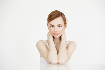 Young beautiful girl with perfect clean skin smiling looking at camera sitting at table over white background. Beauty spa and cosmetology.