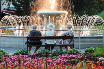 Three older women in a spa talking in front of a park fountain