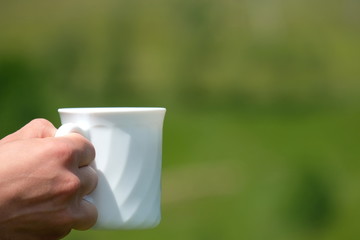 Hand with a white cup of coffee against the background of the mountains