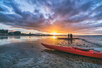 Fototapeta premium Kayaks and kayakers on beach at sunset. Portobello, Edinburgh, Scotland, UK