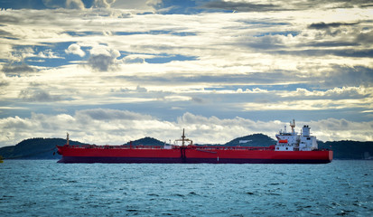 Large cargo vessel anchoring in open sea with island background. Cargo shipping and logistics.