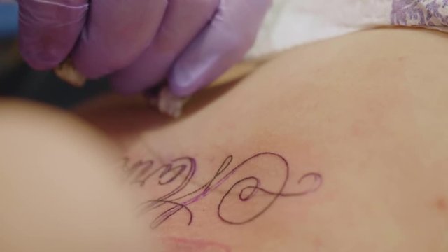 Hands of tattoo artist wearing silicon gloves tattoo girl in studio. Slow motion view