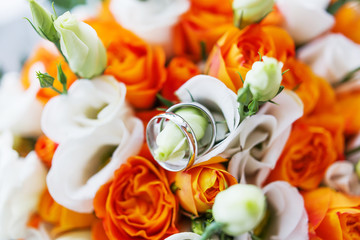 Pair of golden wedding rings inside bridal bouquet. Symbol of love and marriage on orange roses and eustoma (or Lisianthus). Traditional bride's accessory.