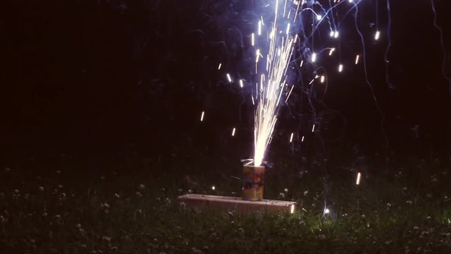 Fireworks for 4th of July resting on wood and sprinkling up in a geyser in darkness
