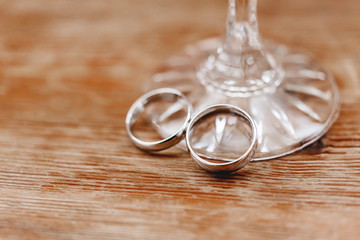 Pair of golden wedding rings on shabby wooden background near stem of glass. Symbol of love, marriage and the fifth ("wooden") wedding anniversary.