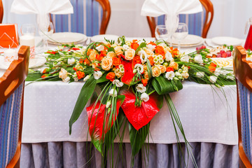 Table set for wedding banquet with cutlery. Floral decorative elements - vases with bouquets of orange roses and white eustoma (or Lisianthus) flowers.