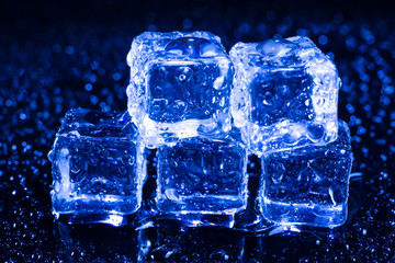 Ice cubes in blue light on black wet table.