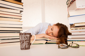 attractive beautiful tired student sleeps on pile of books with a coffee mug on a table
