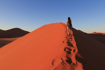Girl on sand dune in desert during sunrise.  Sossusvlei, Namib Naukluft National Park, Namibia - obrazy, fototapety, plakaty