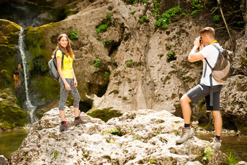 Naklejka premium active young couole hiking in nature resting near waterfalll and taking pictures with camera