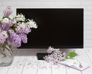 Beautiful white and violet lilac flowers bouquet in vase with opened note-book and black monitor...