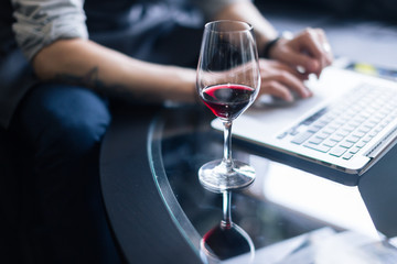 Portrait of senior sommelier sitting in front of laptop at wine cellar and tasting red wine while...