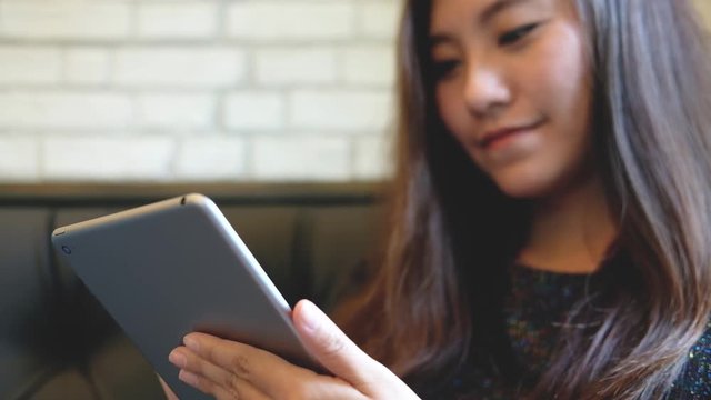 A beautiful Asian woman with smiley face holding , using and typing at tablet pc in modern cafe