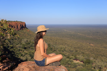 Naklejka premium Girl sitting on stone on the cliff at an forest landscape.