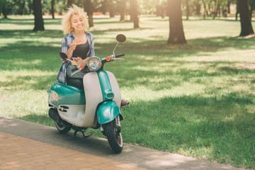 Fototapeta na wymiar Girl Eating on moto scooter or moped. Girl Eating on moto scooter or moped. Happy Young woman holding hot pizza in box. Female student does not have time, he is going to eat on the go.