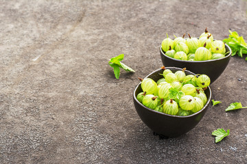 Fresh green gooseberries in a ceramic bowl on a dark background. Top view