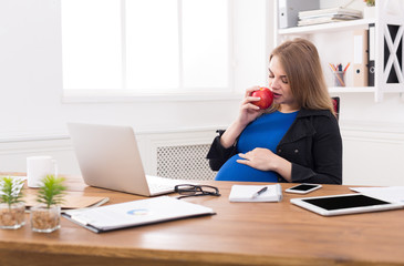 Obraz premium Pregnant woman eating apple in office copy space