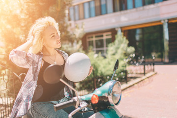 Young cheerful girl driving scooter in in city. Portrait of a young and stylish woman with a moped.