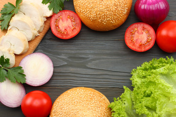 Hamburger Building Kit. round sandwich bun with, tomato, red onion, green lettuce, grilled chicken fillet on dark wooden background. Top view with copy space.