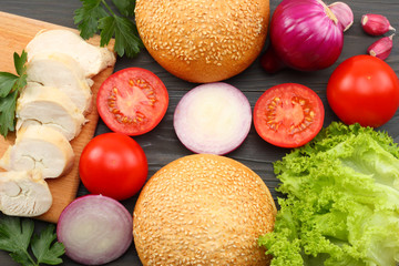Hamburger Building Kit. round sandwich bun with, tomato, red onion, green lettuce, grilled chicken fillet on dark wooden background. Top view with copy space.