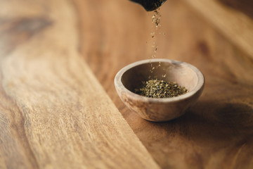 dried provence herb mix falling in wood bowl for seasoning on table