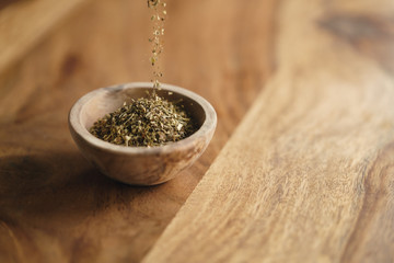 dried provence herb mix falling in wood bowl for seasoning on table