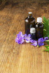 Essential oil of geranium meadow in dark glass containers on wooden background with flowers and leaves. Selective focus.