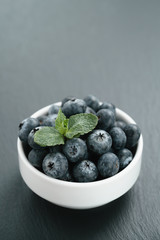 fresh blueberries with mint leaves in white bowl on slate board