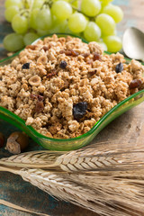 Healthy granola muesli breakfast with grape, nuts and wheat ears in green glass bowl
