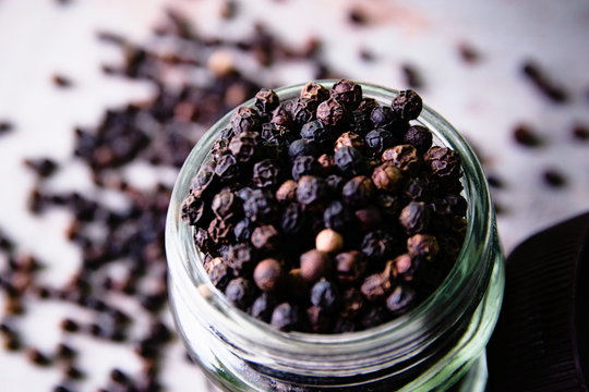 Spicy peppercorns in a glass jar on a wooden background.