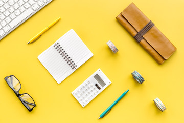 Modern office worker workplace with keyboard, notebook, glasses and pencil case on yellow table background top view