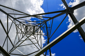 The electricity transmission pylon in daytime outdoors. Electricity tower standard overhead power line transmission tower on the background blue sky and white cloud. 