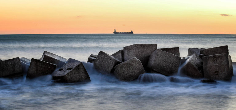 scogli con nave all'orizzonte