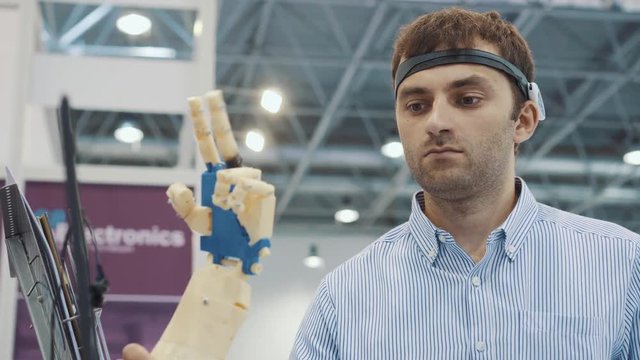 Cybernetic system today. Game industry and motion tracking in cyberspace. Man with innovative spectacles creates movement for mechanical plastic arm. Printing on the 3D printer. Sci Fi and prosthetics