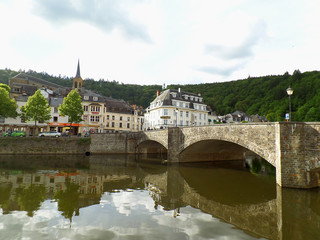Obraz premium Reflections of the old stone bridge and the vintage buildings on Semois river at Bouillon, Belgium 