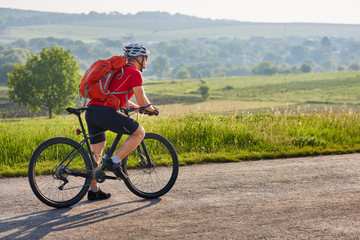 Fototapeta premium Potrtrait of the cyclist on a long road on the countryside against summer landscape.