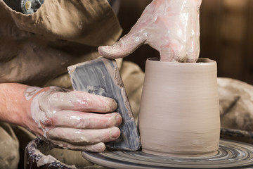 pottery, workshop, ceramics art concept - closeup on male hands sculpt new utensil with a tools and water, man's fingers work with potter wheel and raw fireclay, front close view