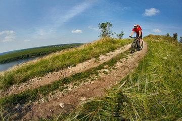 Young cyclist riding the mountain bike on the beautiful summer trail in the countryside against blue sky with clouds.