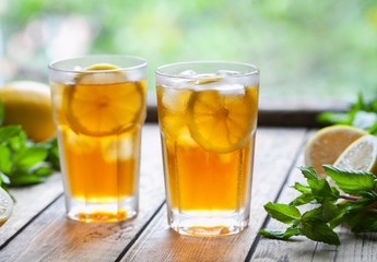 Ice tea with lemon slices on wooden table with a view to the terrace. Cold longdrink or lemonade. Close up summer vitamin antioxidant beverage. A frozen glass. Copy space for text.