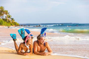 Luxury travel leisure activity watersport fun people relaxing after snorkel swim. Beach couple on summer snorkeling holiday sport activity. Young adults enjoying vacation lying down on sand. - obrazy, fototapety, plakaty