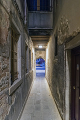 Very narrow cobblestone alley at night in Venice, Italy