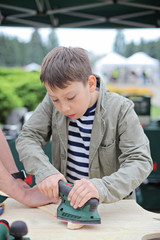 DIY teacher or father teaching son tinkering, using jig saw. Classes for young carpenter polish wood board form using jigsaw. Toy making. Dreaming of future profession. child woodcarving lesson