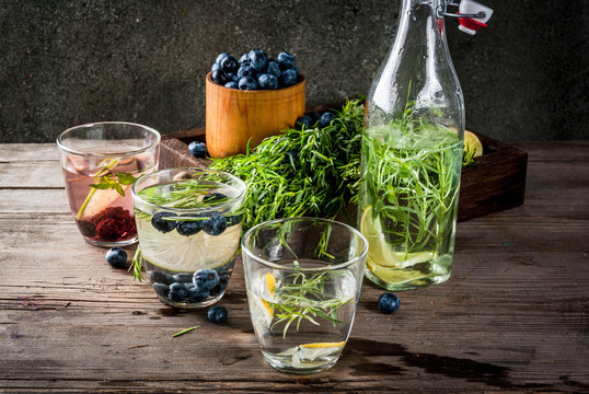 Summer refreshment diet drinks. Infused detox waters in different glasses nd bottles with rosemary, lime and blueberries, lemon and tarragon. Rustic wooden old table Copy space