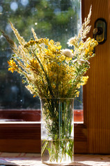 bouquet of yellow wild flowers on the window in a transparent vase