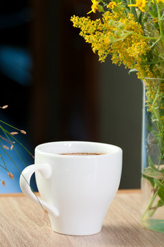 Cup of coffee and a bouquet of yellow wildflowers on the table