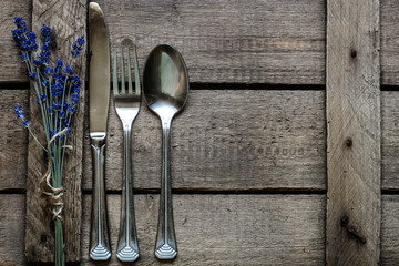 A bouquet of lavender and a set of steel cutlery (fork, spoon, knife) on a wooden background