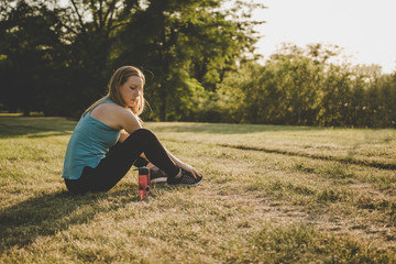 Relaxing outdoor. Young woman sitting in the park and relaxing after running