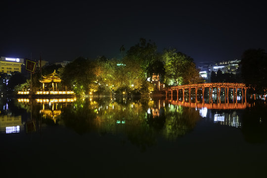 Night view of the Huc Bridge (Morning Sunlight Bridge) on the Hoan Kiem Lake (Lake of the Returned Sword) in historic centre of Hanoi, Vietnam. The bridge reflected in the lake.